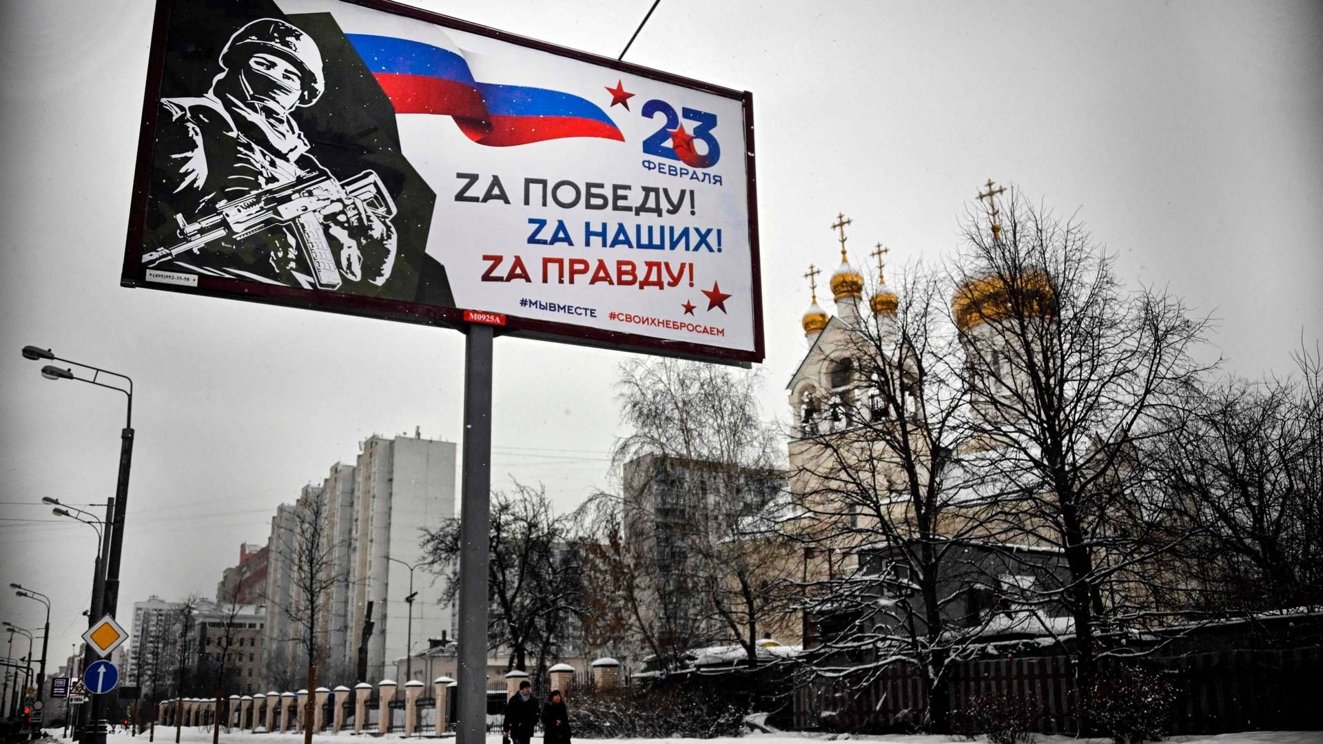 Folk på gaden i Moskva, der går forbi et skilt med teksten "For Sejren! For Vores! For Sandheden!". Moskva, 20. februar, 2023. | Foto: Alexander Nemenov/AFP/Ritzau Scanpix