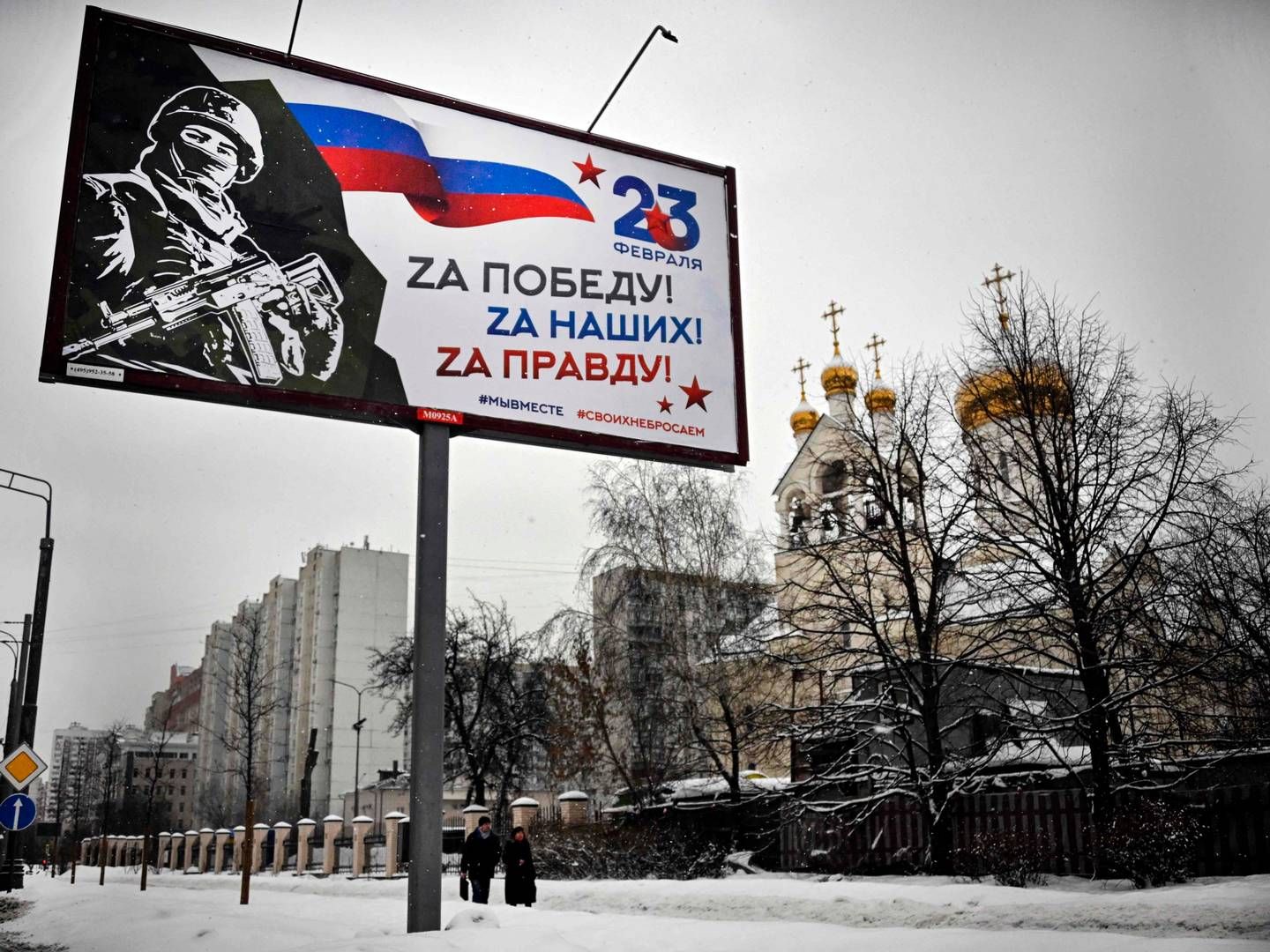 Folk på gaden i Moskva, der går forbi et skilt med teksten "For Sejren! For Vores! For Sandheden!". Moskva, 20. februar, 2023. | Foto: Alexander Nemenov/AFP/Ritzau Scanpix