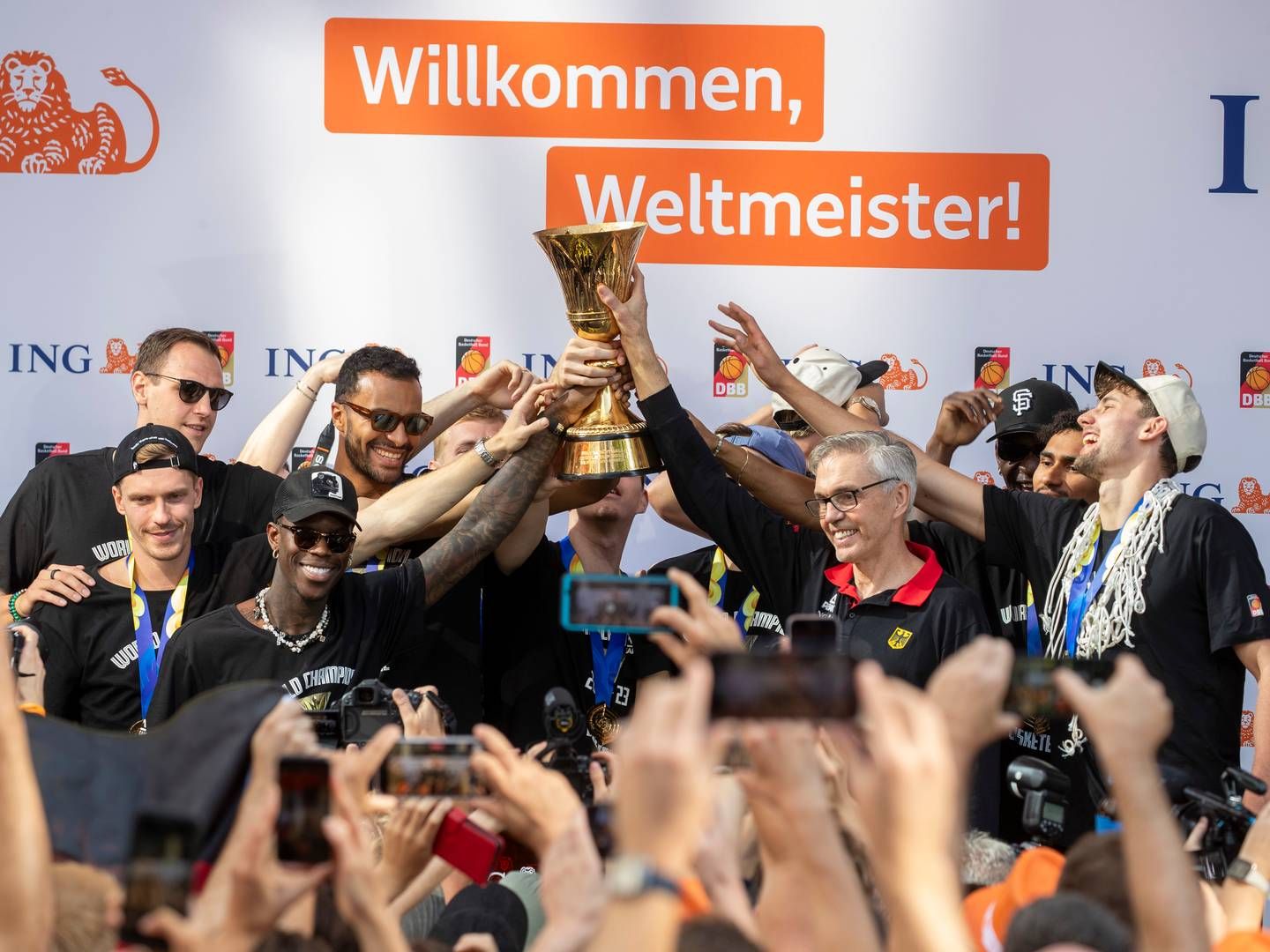 Das Team um Dennis Schröder (3.v.l.) und Trainer Gordon Herbert (4.v.r) mit der WM-Trophäe vor dem Poster von Hauptsponsor ING. | Foto: dpa picture alliance