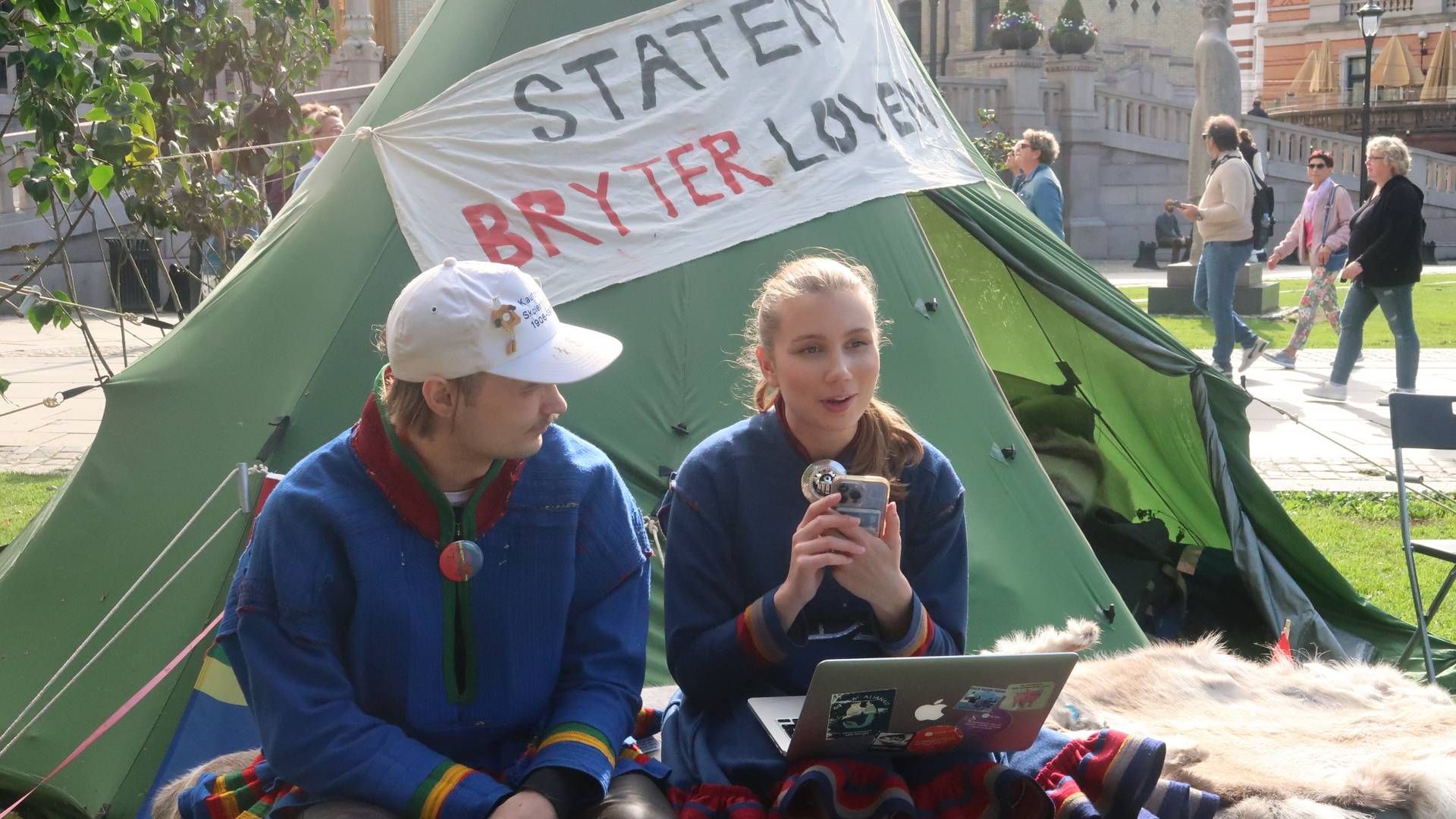 «STATEN BRYTER LOVEN» står det på en lavvu utenfor Stortinget. Her har Mihkkal Hætta (til venstre) sagt han skal bo i protest frem til Fosen-dommen blir fulgt opp. Ella Marie Hætta Isaksen (til høyre) har delt Jusstudentenes Fosenopprop i sosiale medier. | Foto: Linda Sandvik