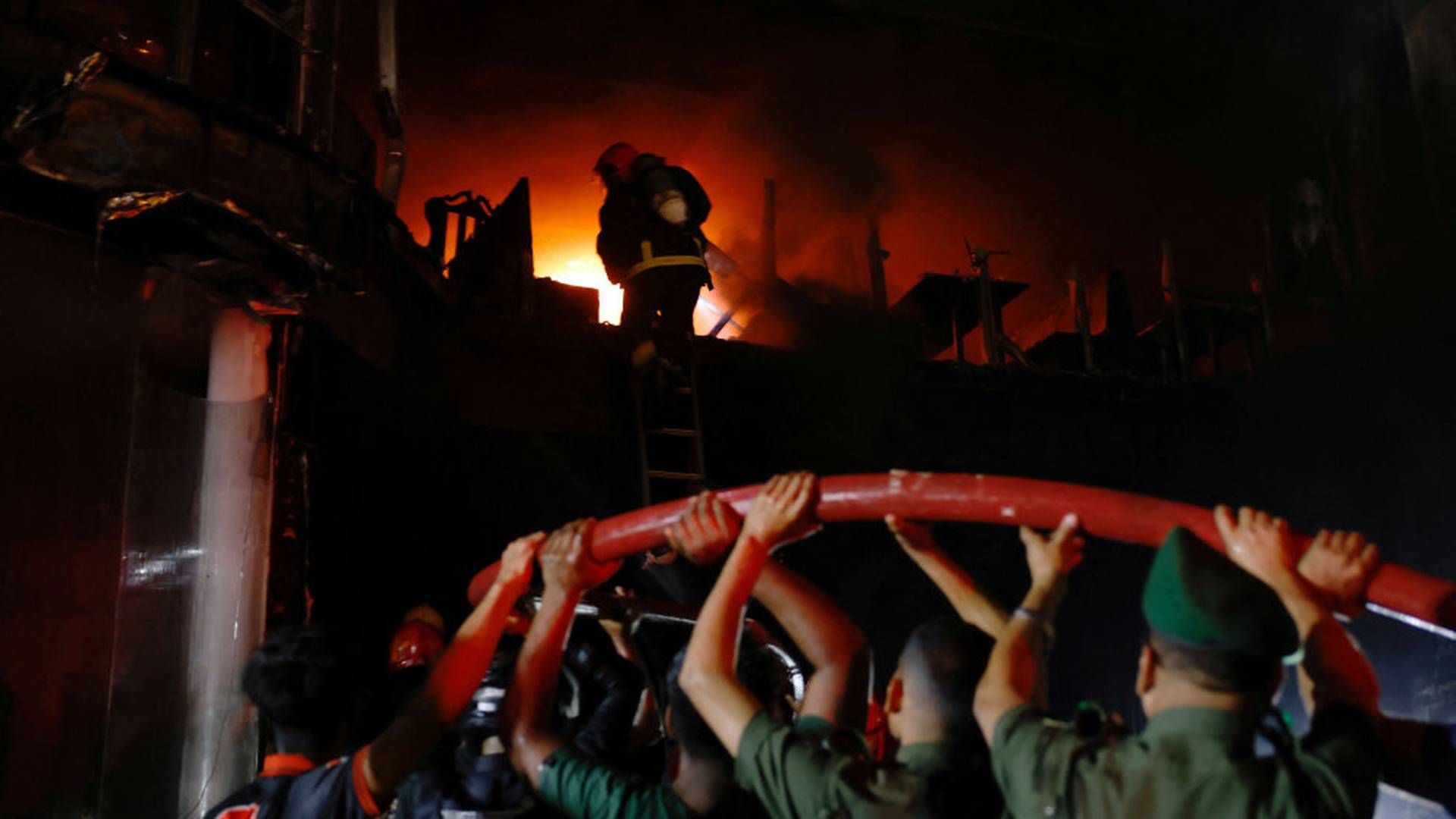 Frivillige bærer på en vandslange, mens en brandmand er i gang med at slukke ilden i den etagebygning i Dhaka, hvor mindst 43 mennesker har mistet livet i en brand. | Foto: Mohammad Ponir Hossain/Reuters