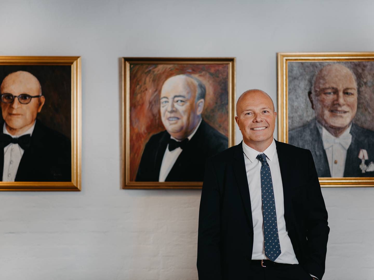 Peter Therkelsen foran malerierne af sin oldefar, farfar og far, der alle har drevet H.P. Therkelsen før ham. | Foto: PR-foto/H.P. Therkelsen