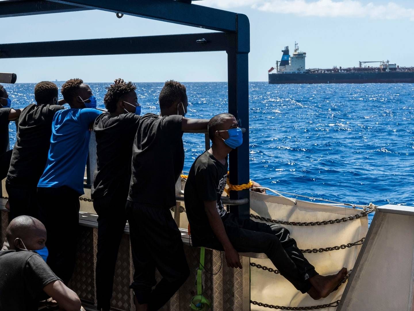People on a passing ship observe Maersk Etienne from afar. 27 migrants including a pregnant woman and a child have now been stuck aboard the ship for more than a month. | Photo: THOMAS LOHNES/AFP / AFP