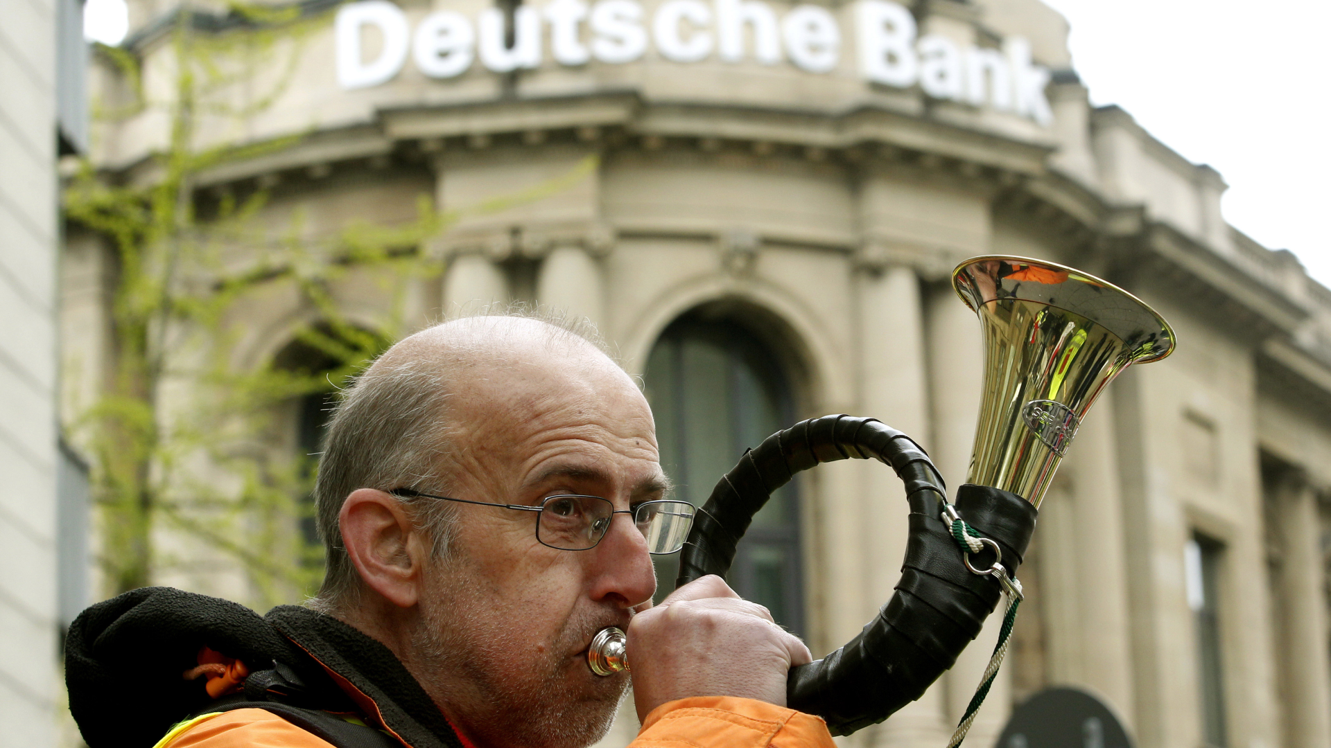Ein Mitarbeiter der Postbank protestiert am 27.04.2015 in Essen vor der Deutschen Bank mit einem Jagdhorn. | Foto: picture alliance / dpa | Roland Weihrauch