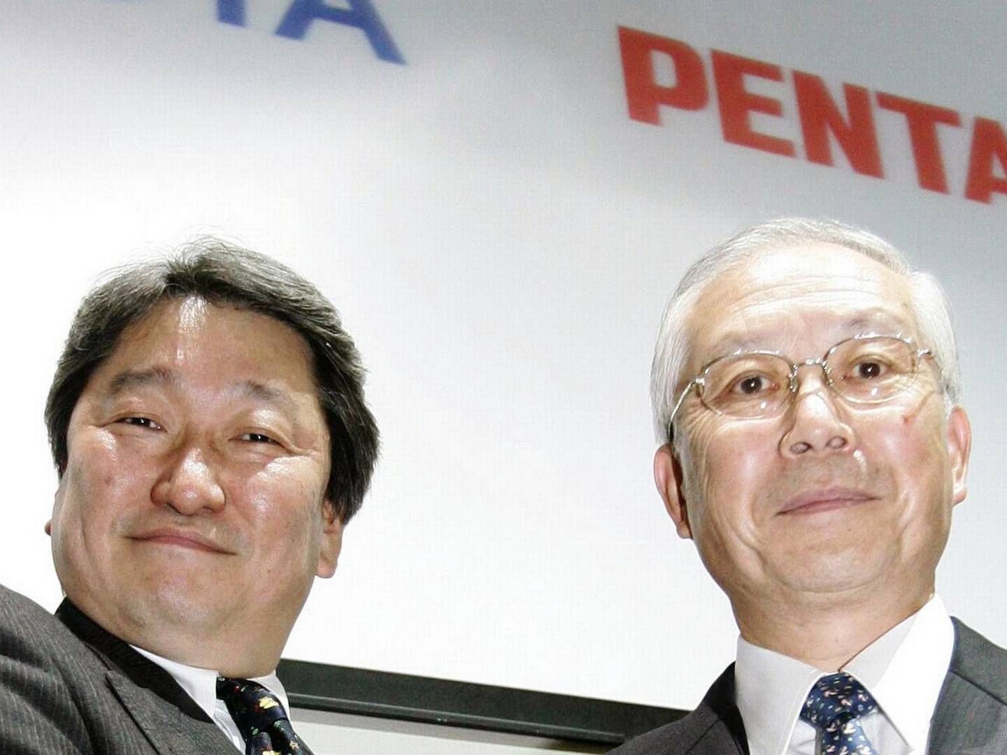 Pentax CEO Fumio Urano and Hoya Corporation CEO Hiroshi Suziki shake hands