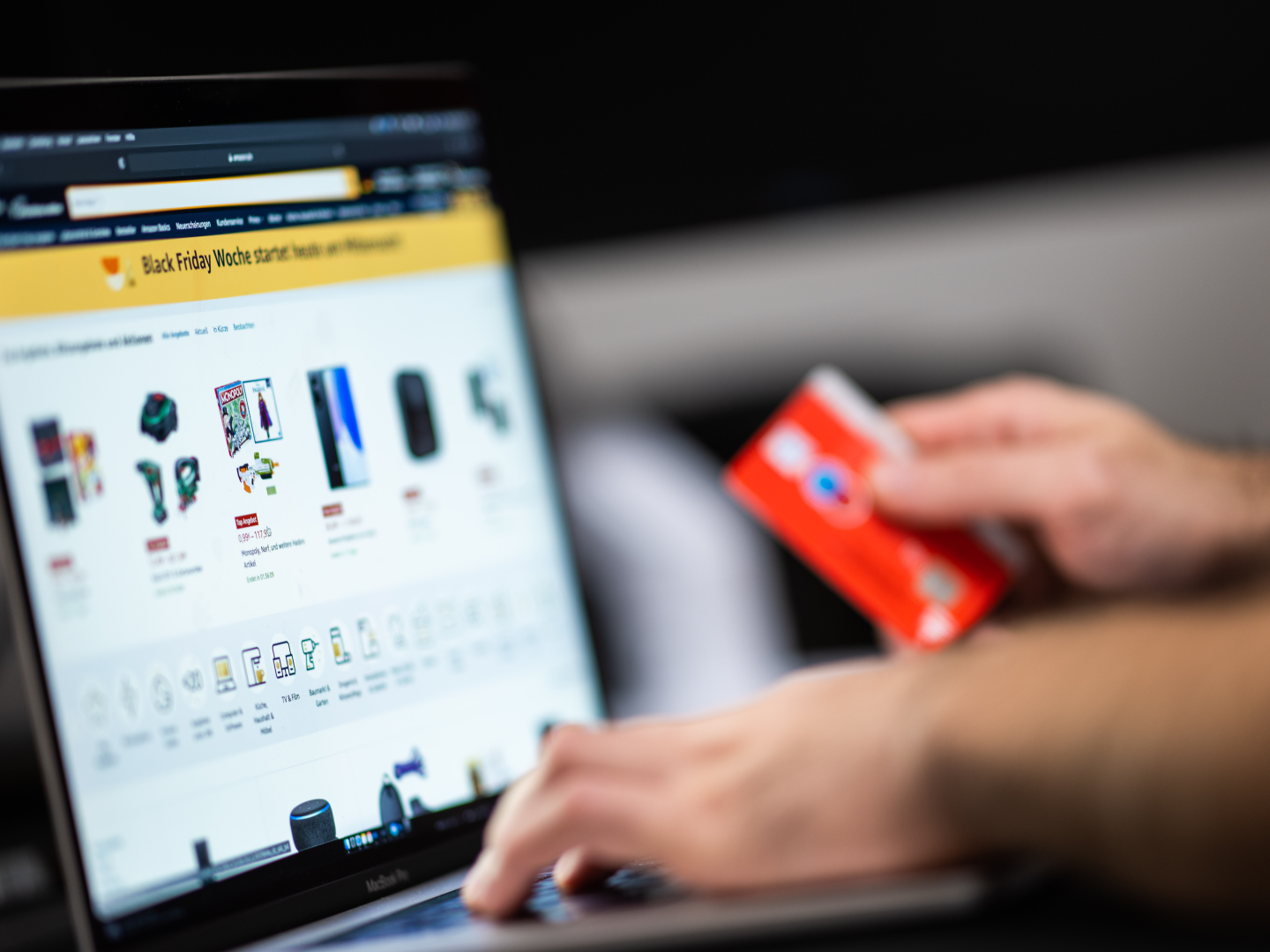 Ein Mann mit einer Bankkarte in der Hand sitzt am Laptop und schaut sich die Black-Friday-Angebote auf der Online-Shopping-Seite von Amazon an. | Foto: picture alliance/dpa | Mohssen Assanimoghaddam