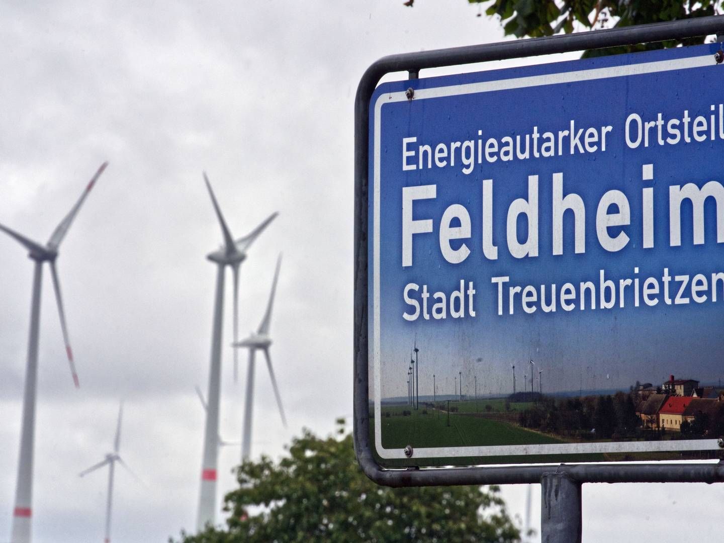 SELVFORSYNT BYGD: Vindturbiner i bygda Feldheim i Tyskland. På skiltet står det "Det energimessig selvforsynte distriktet Feldheim". | Foto: AP Photo/Michael Soh